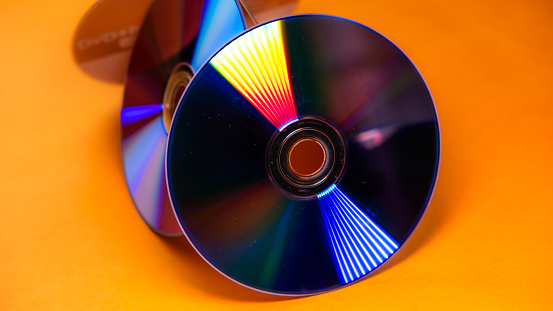 Color refraction and orange background on the back glossy sides of leaning DVDs, side angle, Digital Versatile Disc or Compact Disc