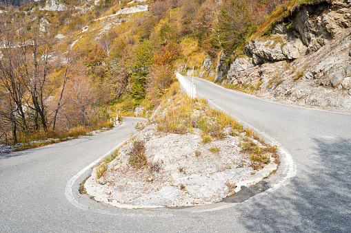 Danger curve on serpentine mountain road, picturesque Alps autumn landscape. Lombardy, Italy. Tourist adventure