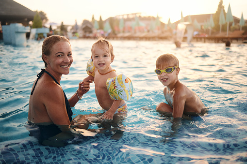 Happy mother swimming with cute adorable baby daughter in swimming pool. Smiling woman and little child, girl of 6 months having fun together. Active family spending leisure and time in spa hotel.