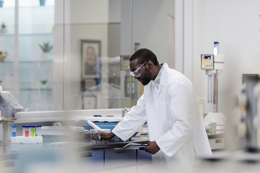 While working in the laboratory on campus, the male chemistry student reads his lap report while conducting an experiment.