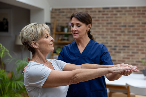 Senior woman doing physical therapy at home with the help of a physiotherapist - healthcare and medicine concepts