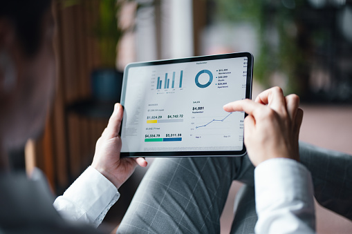 A back view of an unrecognizable Caucasian entrepreneur analyzing some statistics using his tablet while sitting in the office.