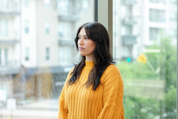 istock Depressed women looks through window on gloomy day 1649071926