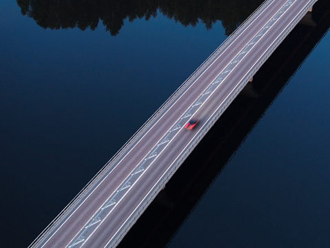 A single car in motion on a bridge crossing a river in the late evening.