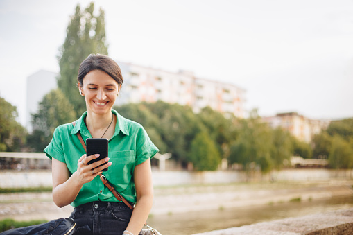 Happy young woman using a smartphone outdoors stock photo