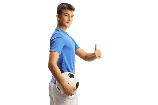 Young football player holding a ball and gesturing thumbs up isolated on white background