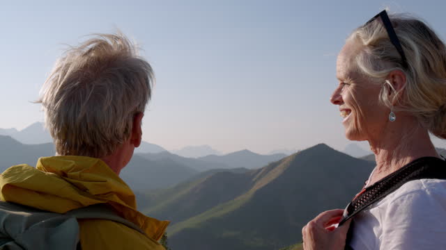 Mature hiking couple look off to mountains from summit viewpoint