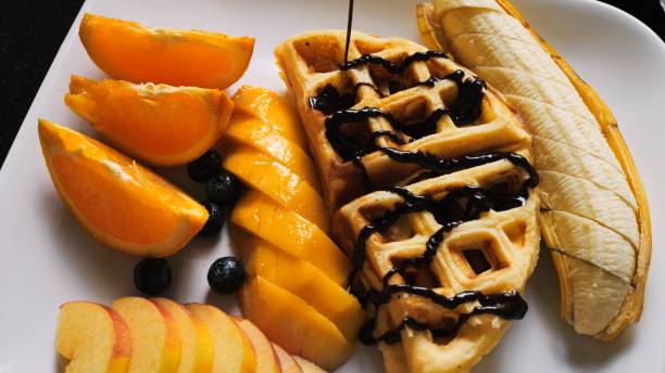 Delectable Breakfast: Drizzling Vienna Waffles and Fresh Fruits with Chocolate Syrup. Enjoy delightful morning feast as rich chocolate syrup is poured generously over Vienna waffles and fresh fruits
