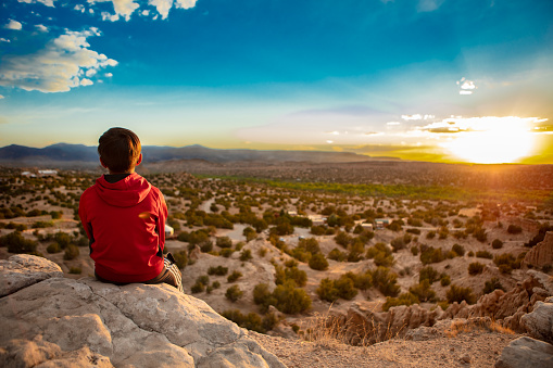 Boy sits on a rock watching the sun set in New Mexico.