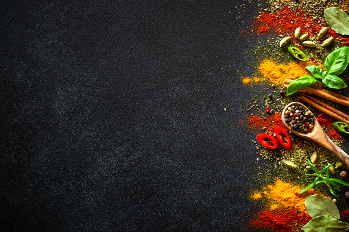 Spices and herbs on black slate background. Pepper, turmelic, dill, cinnamon, basil, rosemary, chilly, cardamom. Top view with copy space.