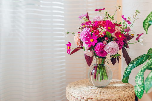 Close up of summer bouquet of pink roses dahlias flowers in vase on straw rattan wicker pad. Interior and decor at home. Space