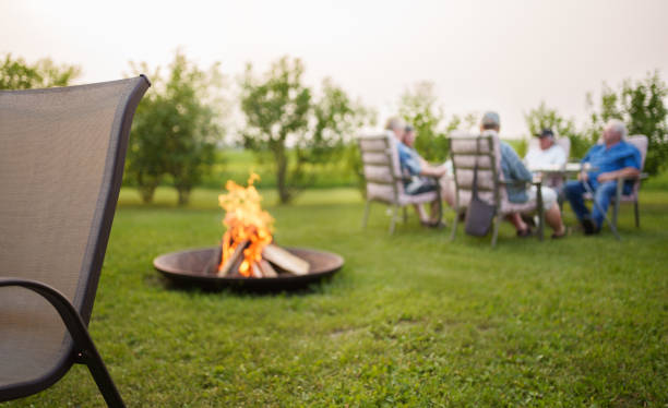 Campfire burning in a fire pit with a group of senior friends sitting in garden chair and talking in the background