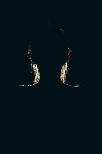 Young woman using mobile phone in darkness of the night. Phone's screen light illuminates her silhouette.