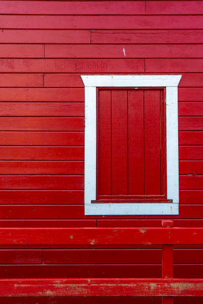 A vibrant red wooden building featuring vertical planks and a simple white window contrasts beautifully against the clear daylight, showcasing unique architectural details.