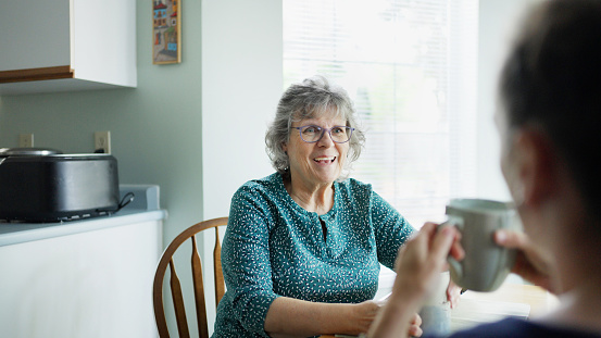 Smiling mature woman talking with her daughter over tea at a kitchen table at home during a visit