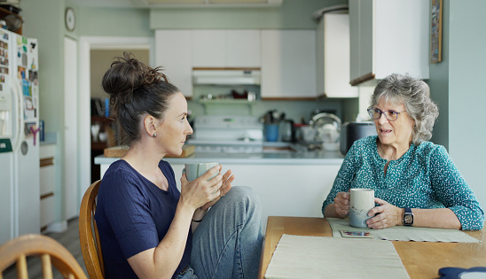 Young woman talking with her mature mother over tea at a kitchen table at home during a visit