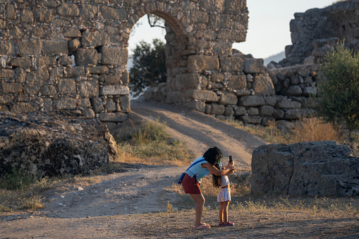 Photo of 5 years old girl photographing her mother with smartphone in historical old ruins of Latmos Herakleia, near Milas, Aydin, Turkey. Shot under daylight with a full frame mirrorless camera.