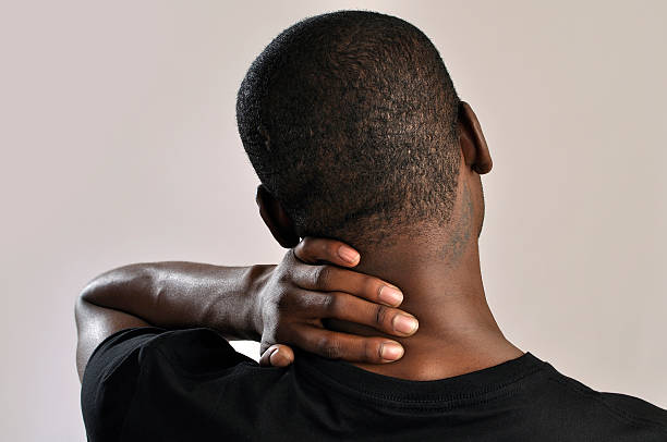Male holding the back of his neck cause of pain Closeup of man rubbing his neck with hand as he aches with pain in the neck on grey background back of head photos stock pictures, royalty-free photos & images