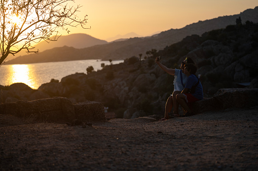 Photo of mother and 10 years old son standing by lakeshore and watching sunset. Shot under daylight with a full frame mirrorless camera.