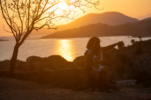 Photo of mother and 5 years old daughter watching sunset by lakeshore. Shot with a full frame mirrorless camera.