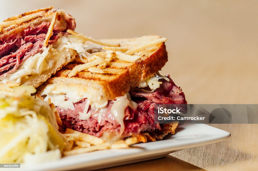 A corned beef sandwich on a plate A "New Yorker" sandwich with Corned Beef and Pastrami, topped with potato sticks. Reuben Sandwich Stock Photo