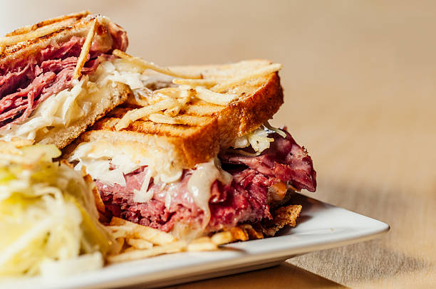 A corned beef sandwich on a plate A "New Yorker" sandwich with Corned Beef and Pastrami, topped with potato sticks. reuben sandwich stock pictures, royalty-free photos & images