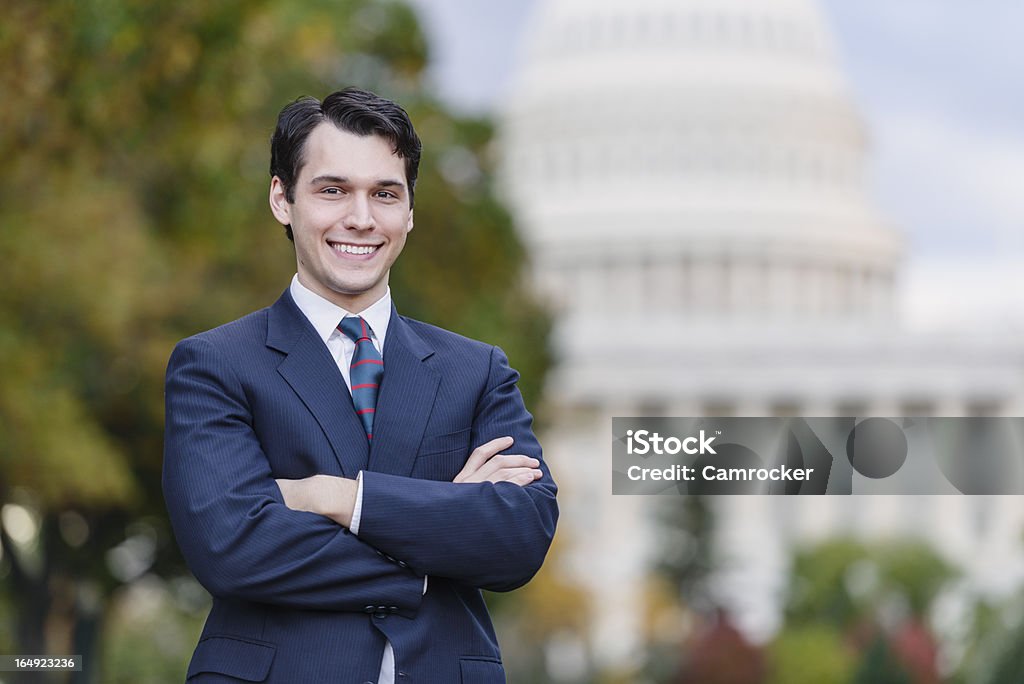 I Know How To Fix Washington A young politician, staffer, or lobbyist holds with his arms folded, with a confident smile. The United States Capitol building is in the background. Politician Stock Photo