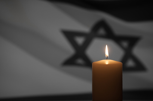 Burning candle on Israel flag background. International Holocaust Remembrance Day, January 27.