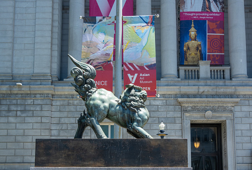 San Francisco, CA, USA - July 12, 2023: Bronze statue of a lion in front of Asian Art Museum facade with its columns and colorful banners promoting its treasures