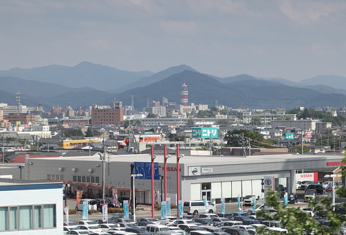 Morioka, Japan - June 10, 2023: High angle view of businesses near National Route 4 in Iwate Prefecture. Spring afternoon with clouds over the mountain range.