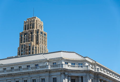 San Francisco, CA, USA - July 12, 2023: Beige tall UC Hastings tower peeks over top floor of white Federal Office building on United Nations Plaza under blue cloudscape