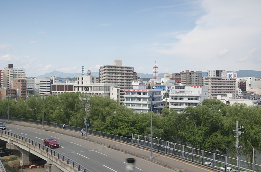 Morioka, Japan - June 10, 2023: Traffic and pedestrians travel along an elevated Route 220 outside Morioka Station near Kitakamigawa Park by the Kitakami River. Spring afternoon in Iwate Prefecture.