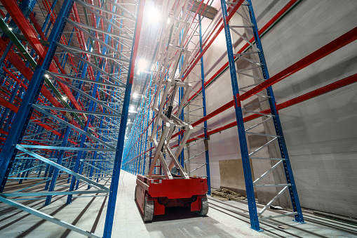 Hydraulic lifting platform on the construction site of an industrial building. A scissor elevator inside a huge warehouse is used to install tall metal shelving units