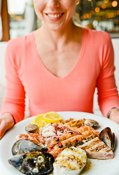 happy smiling mature woman with plate of grilled seafood - mature woman having fish bildbanksfoton och bilder