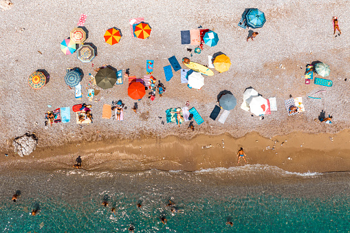 Partly crowded beach captured with a drone directly from above during one hot summer day with all the sun-beds, towels and parasols while emerald colored water was lapping the sandy beach.