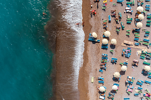 One summer afternoon on the exotic beach washed by the beautiful emerald water seen directly from above and captured with a drone with all the beach equipment like sun-beds, towels and umbrellas.
