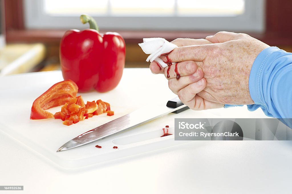 Kitchen Accident with Knife and Blood A senior woman holds gauze to a finger she cut with a knife while slicing a red pepper.  Finger is dripping blood. Wound Stock Photo