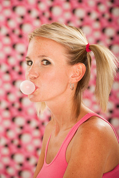Blond woman in pink blowing bubblegum bubble