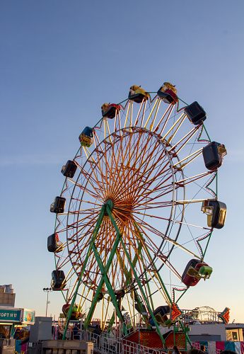 A brightly lit large Farris wheel with caged cars is against a bright blue sky.