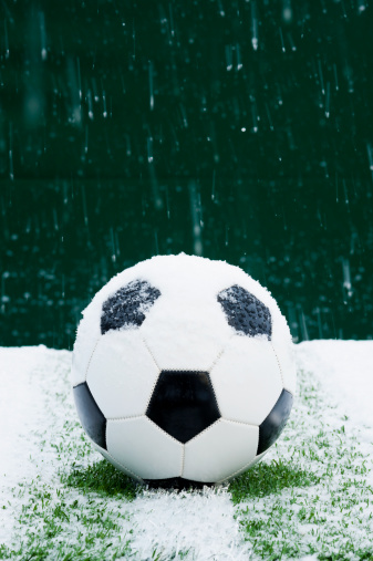 A snow covered soccer ball sitting at the halfway line with a green wall background