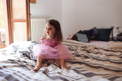 little girl in a pink dress sitting on the bed.