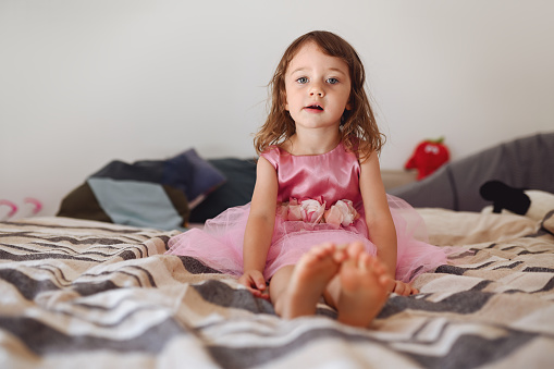 portrait of a cute little girl sitting on the bed.