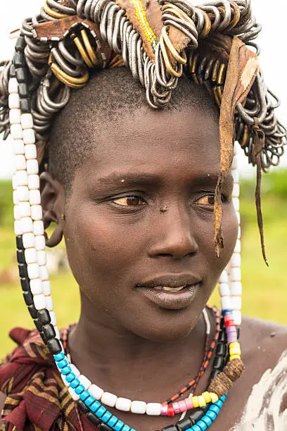 Portrait of a young, beautiful traditional Mursi tribe woman wearing ornamental jewelry on her head and neckleses.  It is south Ethiopia near Kenya, East Africa as part of Mago National Park.