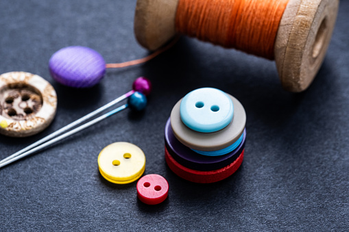 Bright buttons, spool thread and sewing pins on gray background