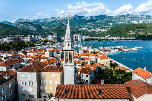 An amazing scenery of the Bell Tower of the Church of Sveti Ivan (St. John) in Budva surrounded with old buildings and houses seen from a drone perspective during one beautiful summer day.