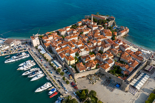 The town of Budva with its old buildings and ancient churches and Budva marina with yachts captured with a drone from a high-angle view looking like a post card surrounded by the blue waters of the Adriatic Sea.