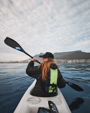 Cape Town, South Africa – April 19, 2023: A closeup of a Young, blonde girl kayaking with Table Mountain in the background Cape Town, South Africa