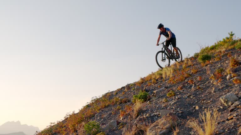 Male mountain biker traverses steep slope above distant mountains