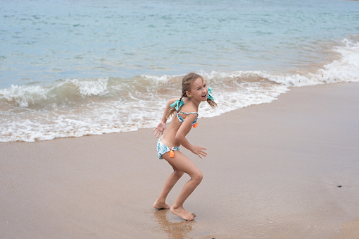 Little girl at the beach vacation, showing thumbs up and looking at the camera