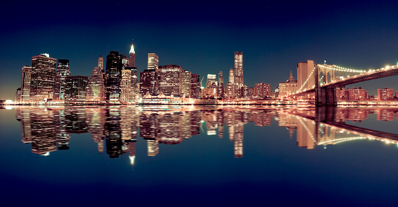 Skyline of Manhattan with Brooklyn bridge reflected on east river in NYC. 